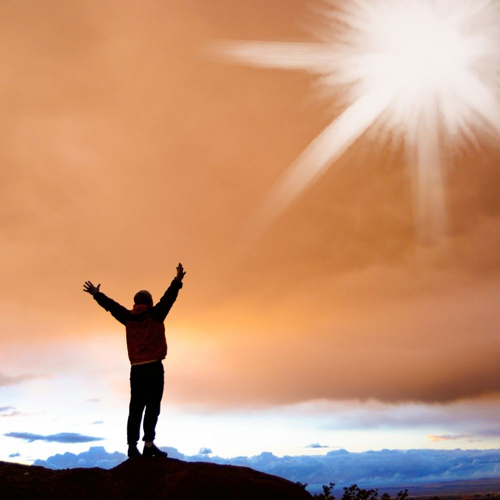 A professional stands on a hill with arms raised towards sunrise, symbolising leadership in governance, legal, and compliance solutions.